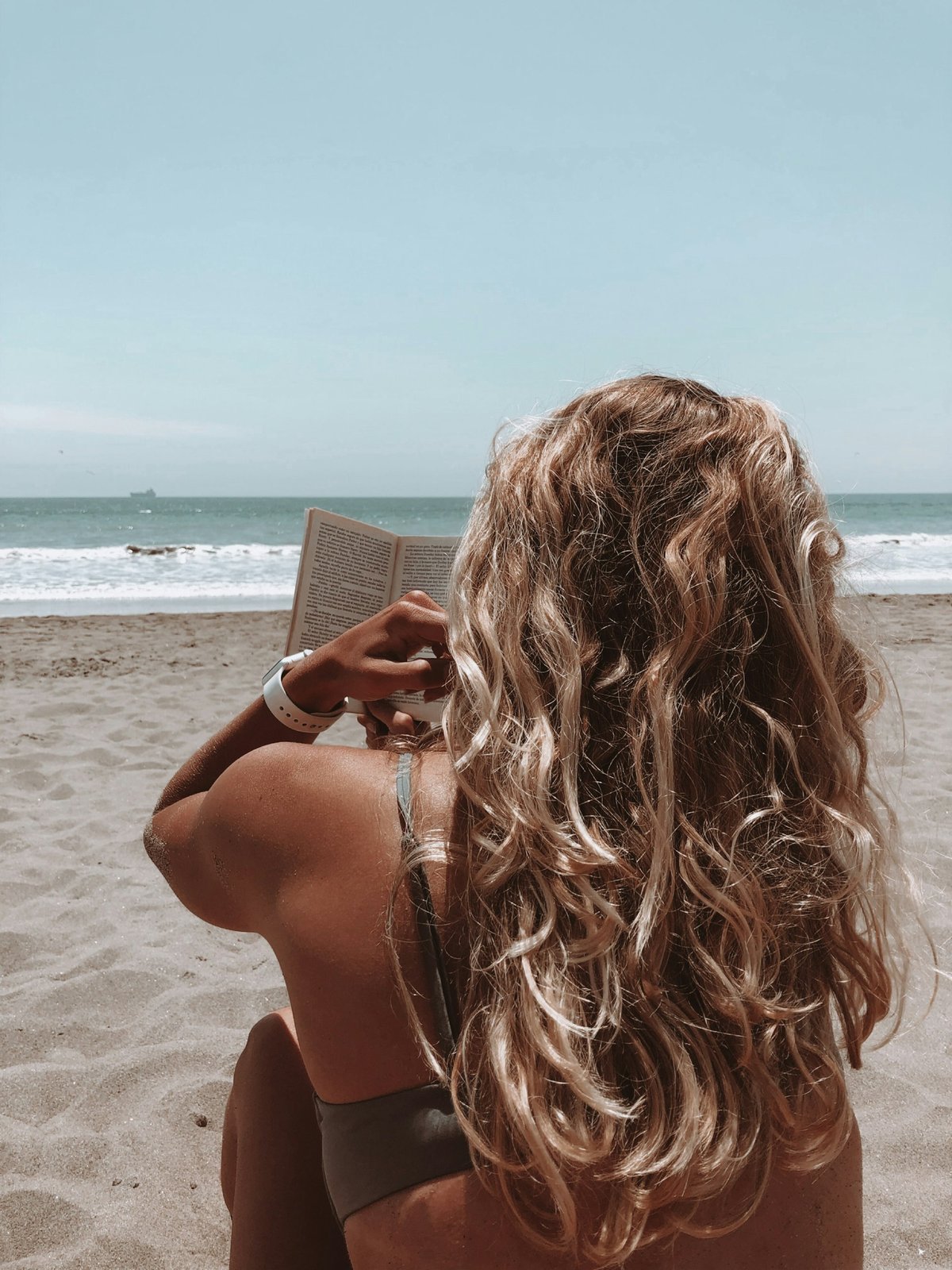 Sun-lightened balayage hair on a bright beach, where strong UV breaks down hair colour fastest